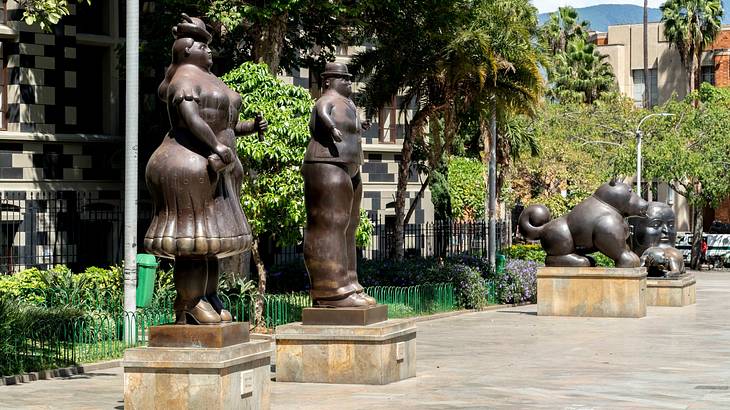 Bronze contemporary art statues in a square with trees behind them