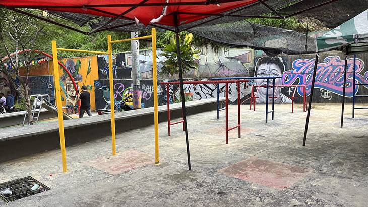 Metal gym bars and a playground under a red awning with graffiti at the back