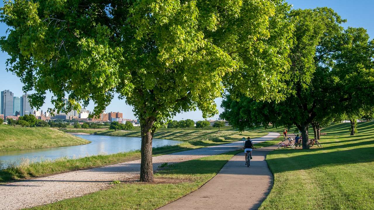 A path with a person on a bike on it next to a river and greenery