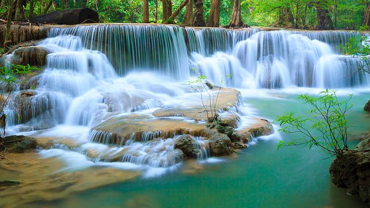 A turquoise pool of water with a waterfall and trees in the background