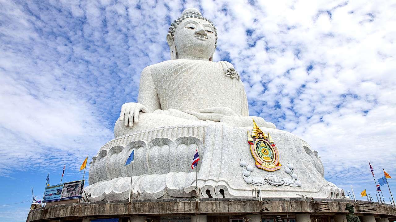 A large white marble Buddha statue against a blue sky with clouds from below