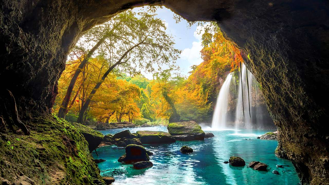A small waterfall cascading amongst rocks and trees in autumn colors through a cave
