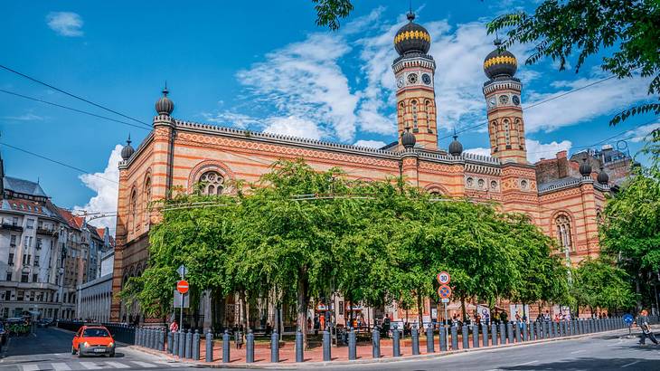 A terracotta synagogue with two towers near trees and a sidewalk