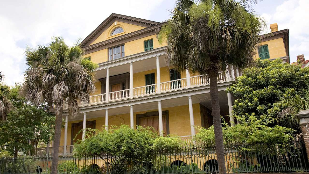 A yellow house with white columns and balconies surrounded by trees
