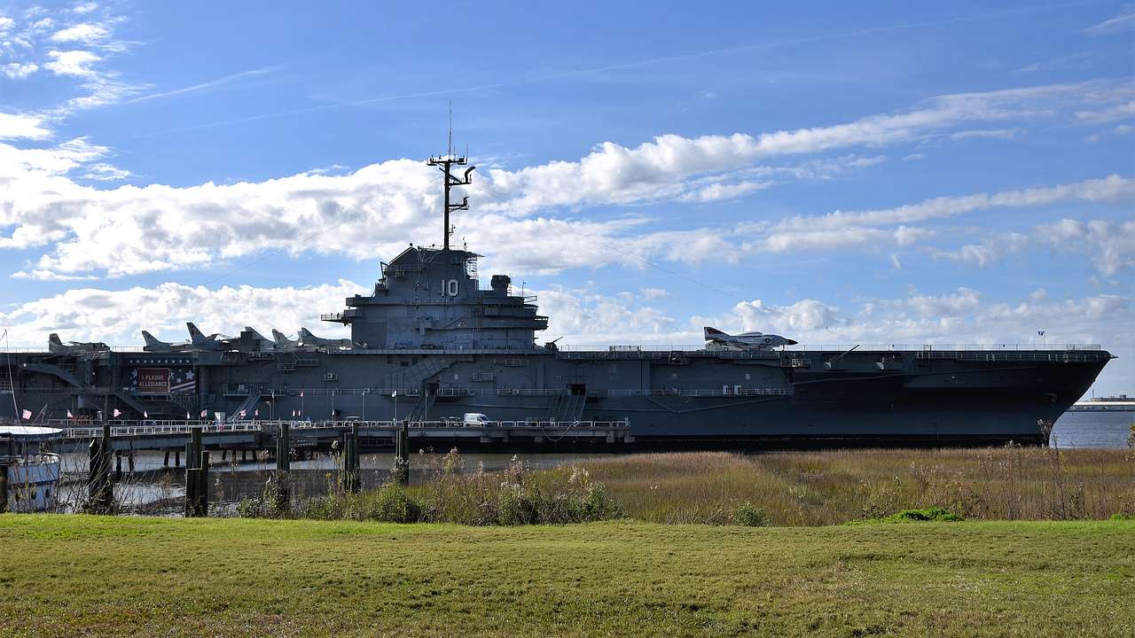 An old aircraft carrier moored by a port near a lawn