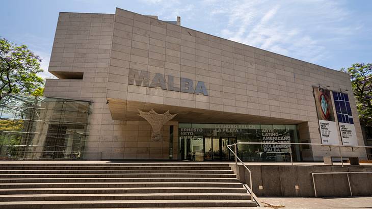 Entrance of a massive building with a staircase and trees beside it on a sunny day