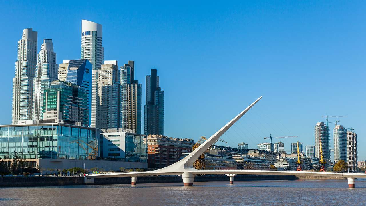 White asymmetrical bridge on the water with huge buildings in the background