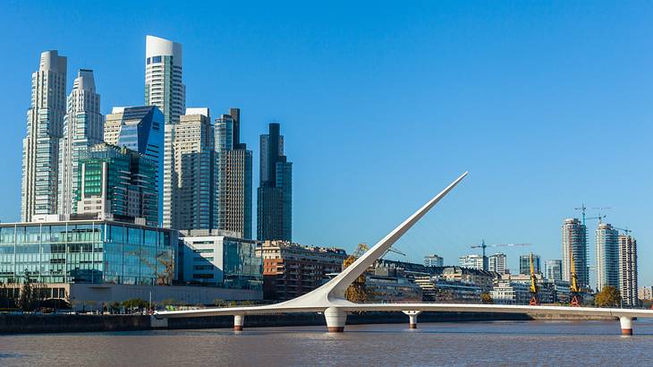 White asymmetrical bridge on the water with huge buildings in the background