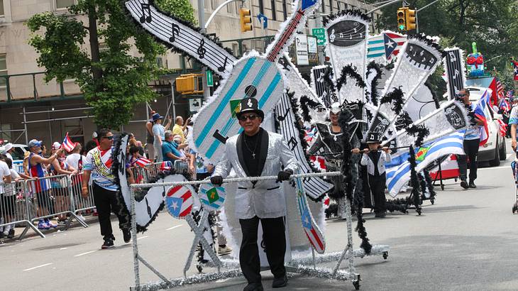 A parade led by a man dressed in a suit pushing a music-themed structure