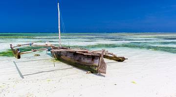 An old fishing boat on the shore of a white-sand beach with light, lapping waves