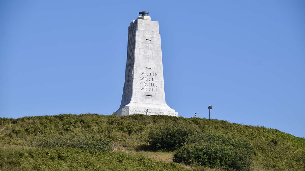 A large grey monument on top of a grassy hill on a nice day