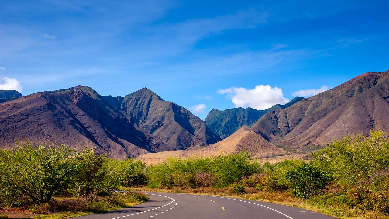 Mountains with a winding road and greenery in front under a blue sky