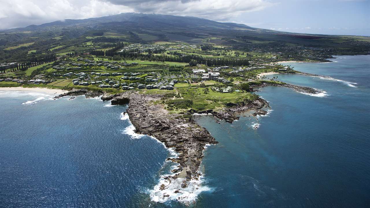 An aerial view of Maui with ocean, rocky coastline, and green land below