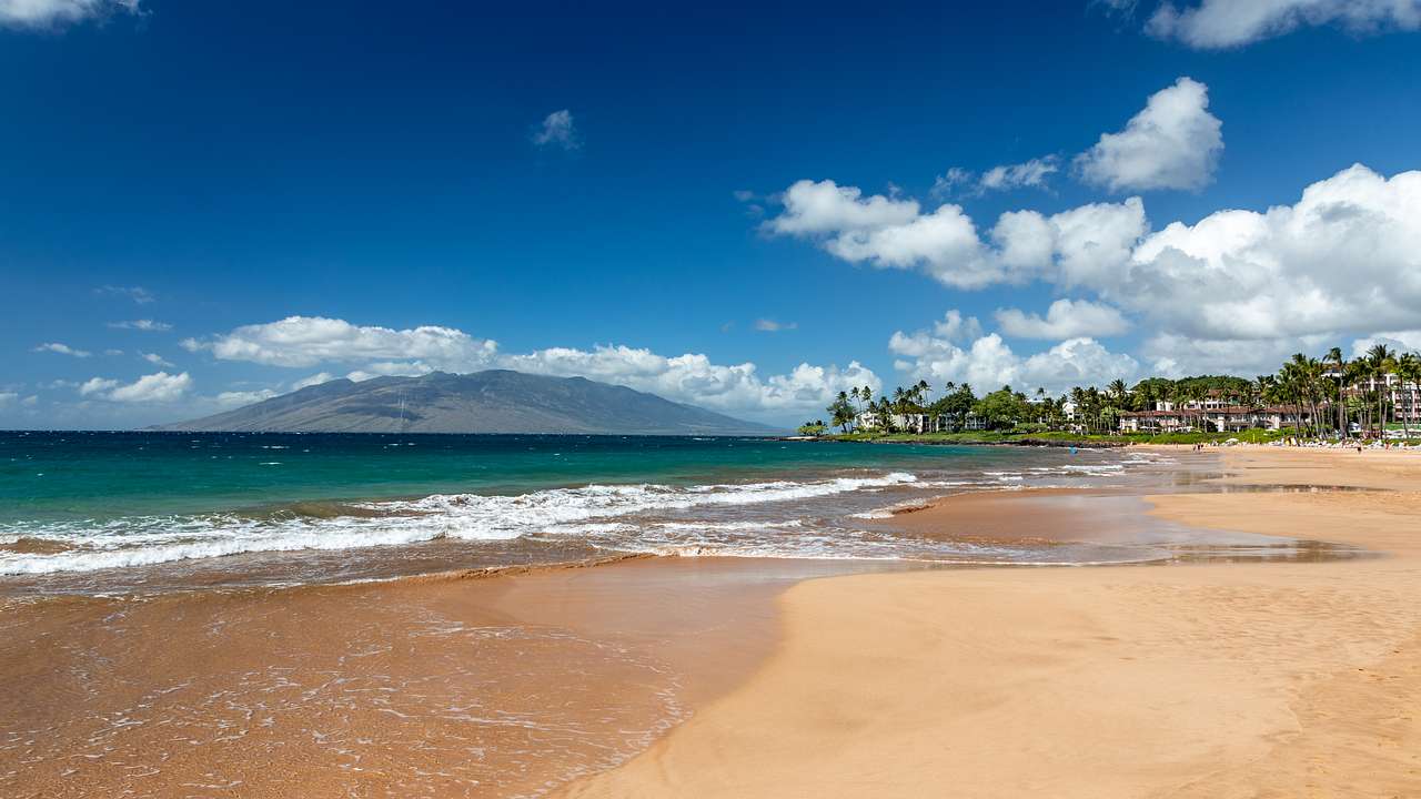 A sandy beach with waves crashing and a mountain and town in the background