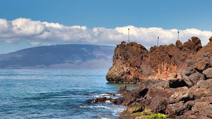 Large rocks beside the sea with spears planted on top on a nice day