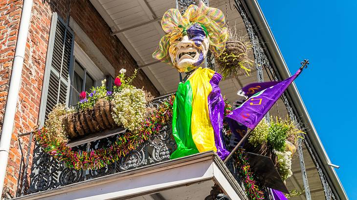 A balcony with a metal railing, flowers, a purple flag, and a colorful mask