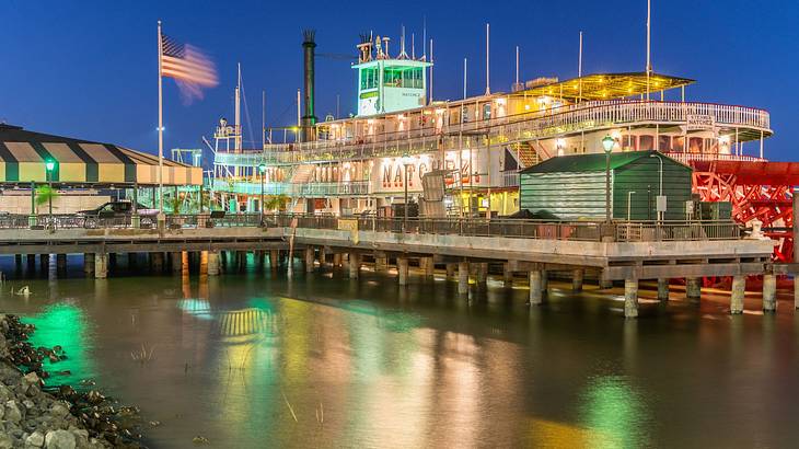 A steamboat on the water with its lights on, parked at a covered pier at night