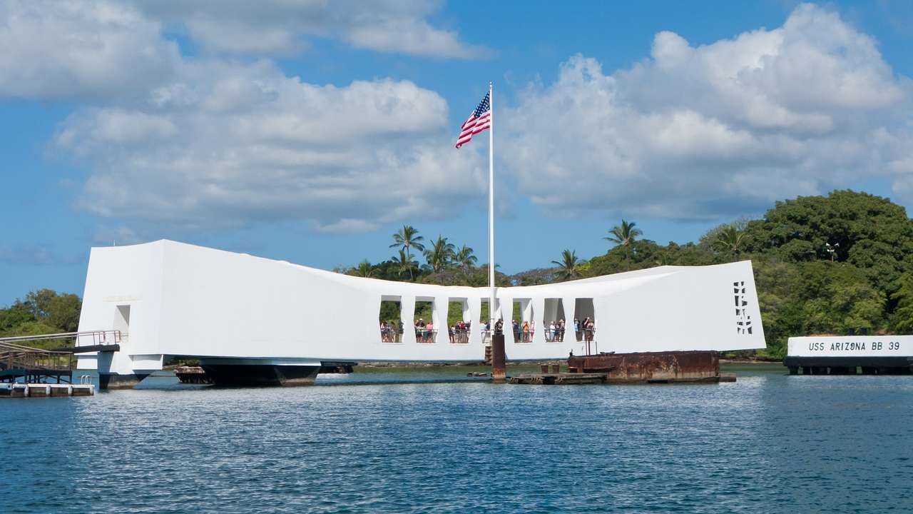 A white monument building with an American flag sitting on the water