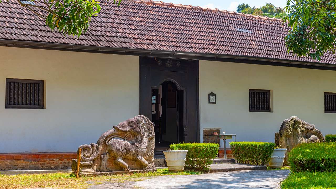 A long, one-story building with a wooden door and two statues carved on rocks