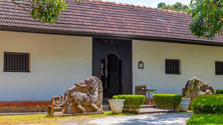 A long, one-story building with a wooden door and two statues carved on rocks
