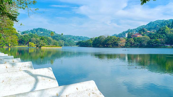 White arched stones and trees lining a calm body of water against tree-covered hills