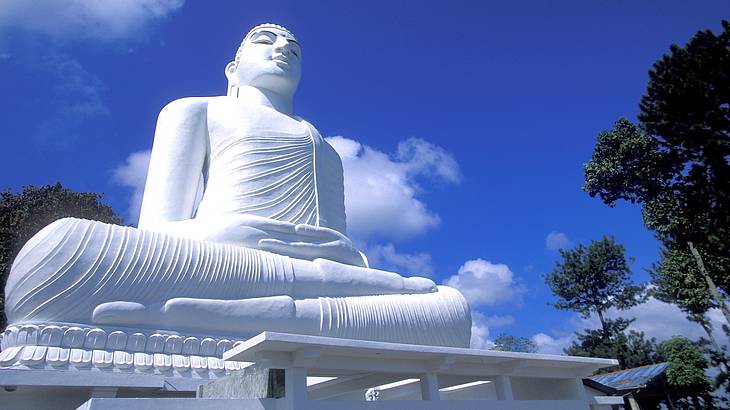 A huge white buddha statue against a partially cloudy blue sky from below