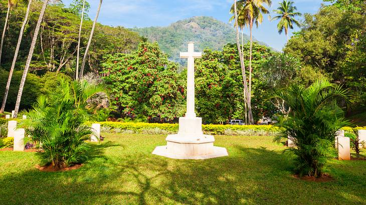 A war cemetery with a tall white cross and tombstones surrounded by lush nature