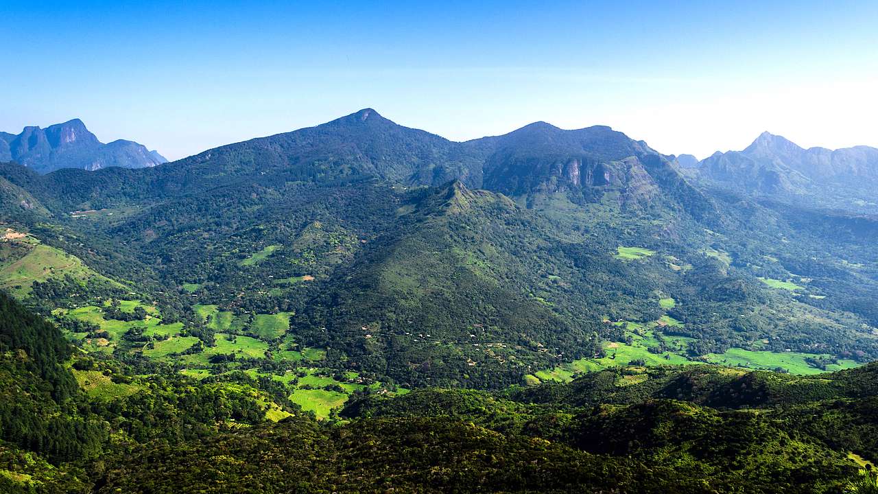 A panorama of lush mountains with fields at the base under a blue sky