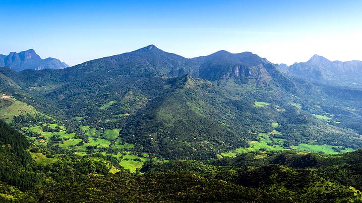 A panorama of lush mountains with fields at the base under a blue sky