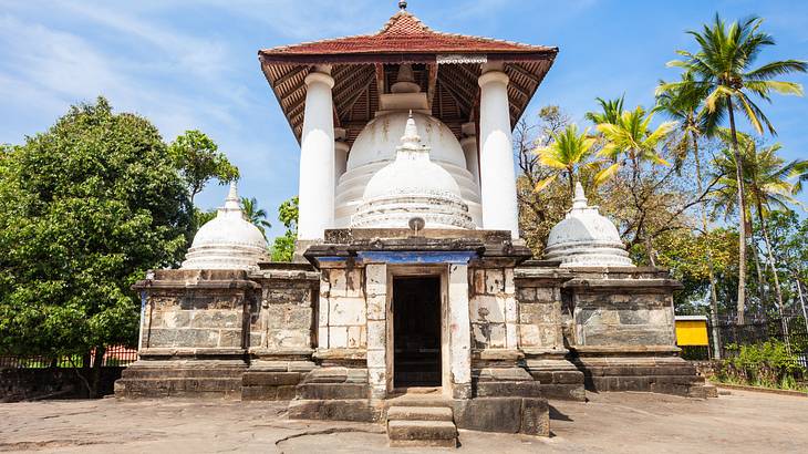 A stone temple with white domes and a brick top and trees around