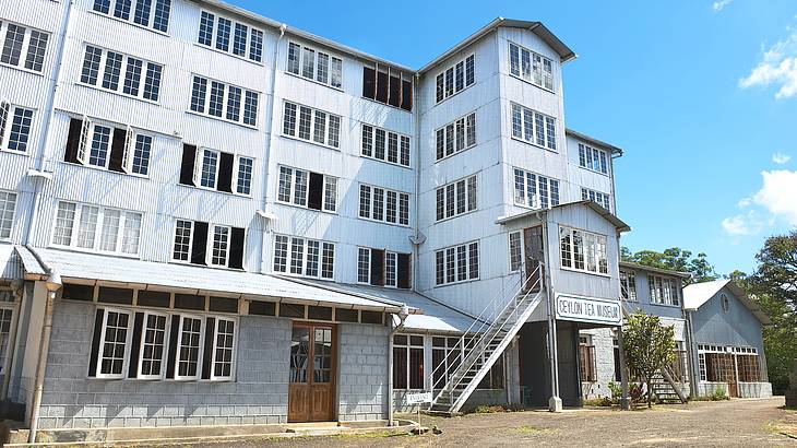 A white building with stairs on the side with trees behind it