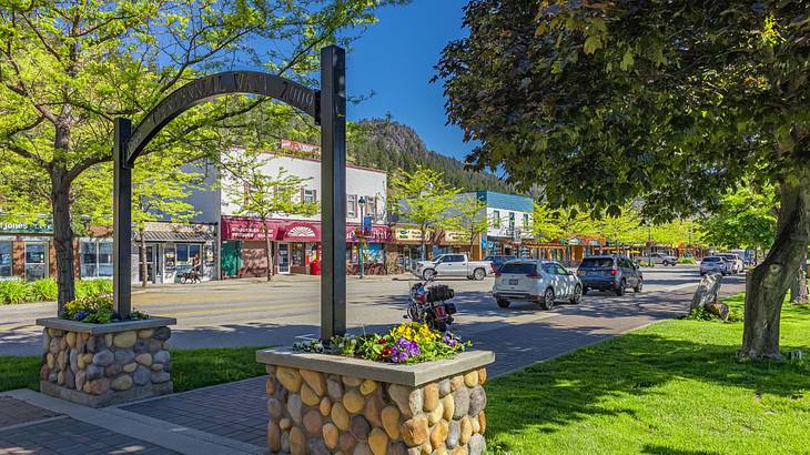 An arch by a small park and a road with shops on it