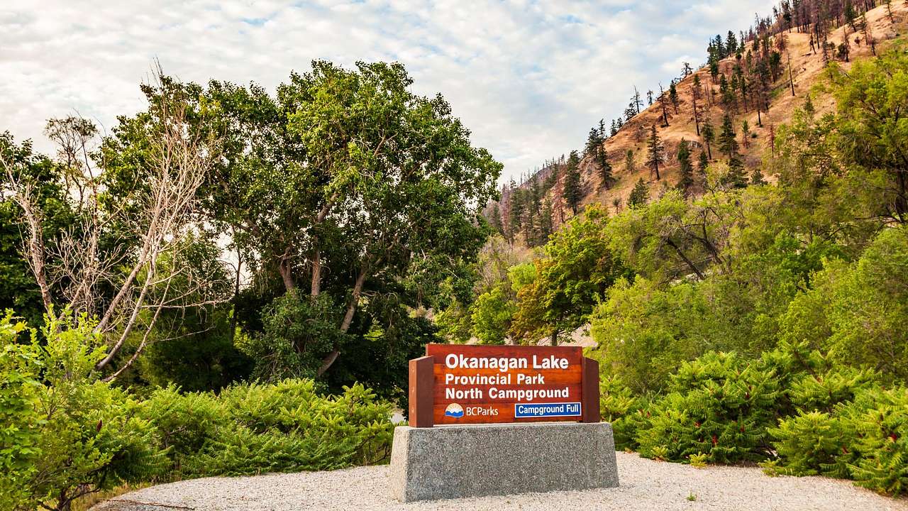 A sign for the park and campground with trees and a mountain in the background