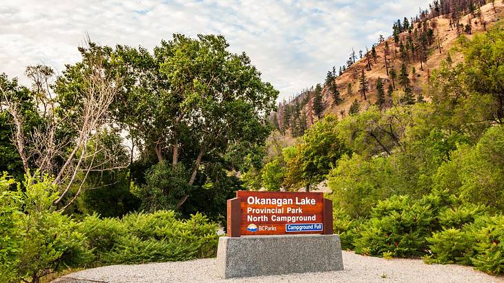 A sign for the park and campground with trees and a mountain in the background