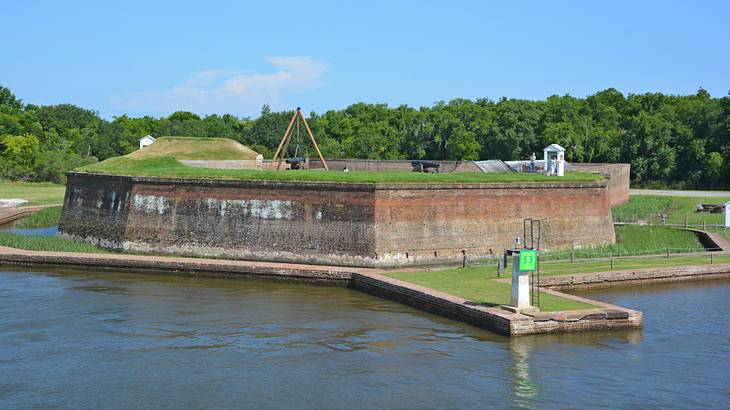 An old fort on a lake, surrounded by grass and trees under blue sky