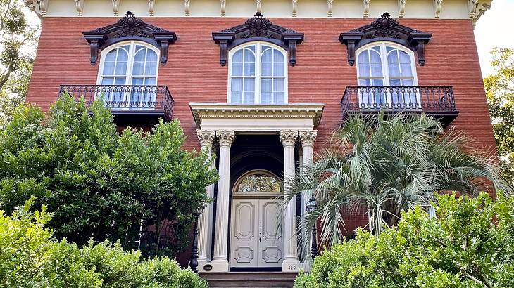 A red brick mansion with a path to the front door and greenery in front