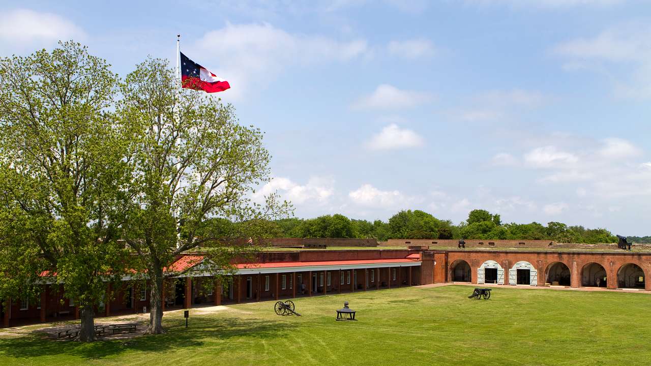 A green lawn next to a red brick building, trees, and a flagpole