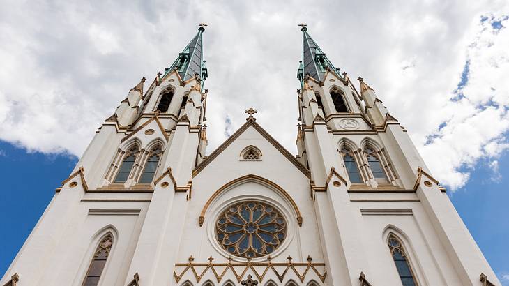 A view from below of a white church with two spires under a cloudy sky
