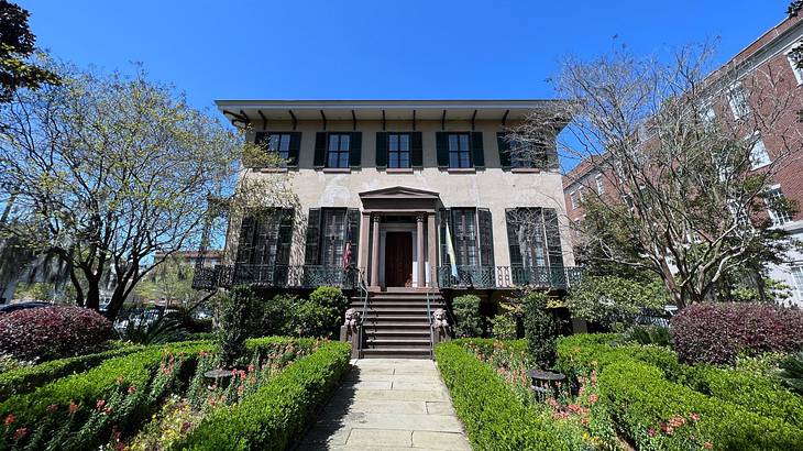 A mansion with a walkway and a front garden full of bushes, flowers, and trees