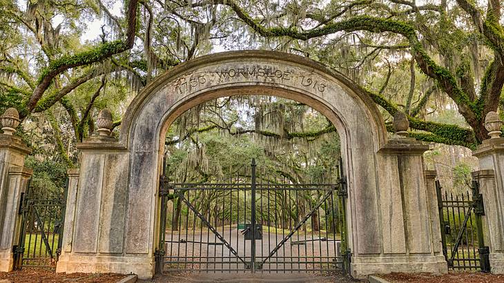 An arched stone and iron gate with a path running through and trees surrounding