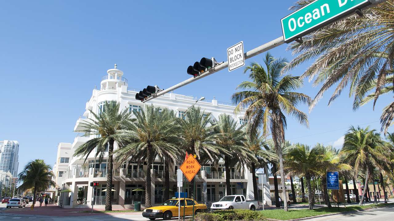 Traffic lights with signage at an intersection next to buildings and palm trees