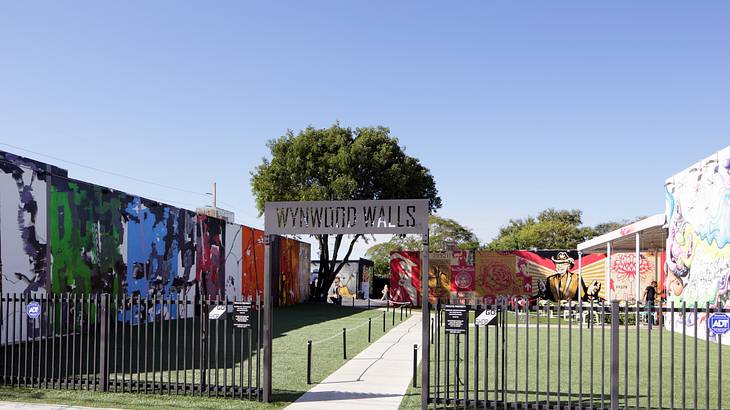 A plot of land with a fence, a sign, and numerous murals on the walls on a nice day