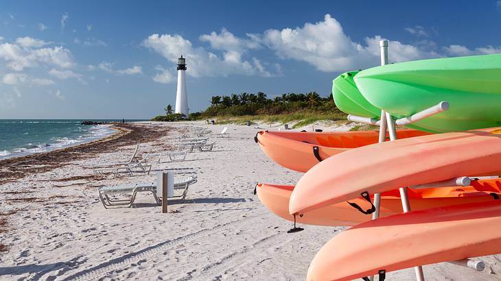 Stacks of plastic canoes on a sandy beach with a lighthouse in the background