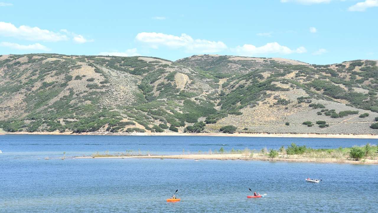A lake with people kayaking on it and a greenery-covered mountain behind it