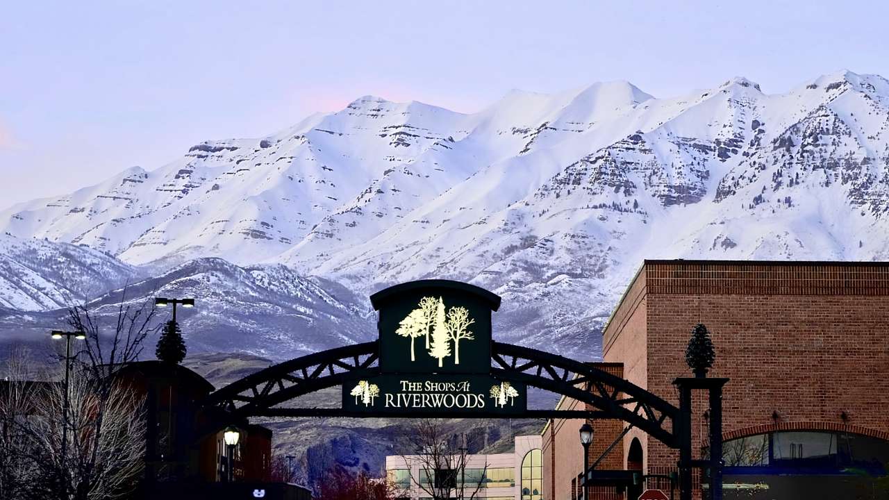 A black arched entryway with a sign, buildings, and a mountain range in winter