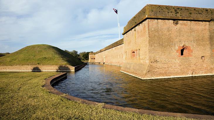 A fort surrounded by a canal and greenery under a cloudy sky