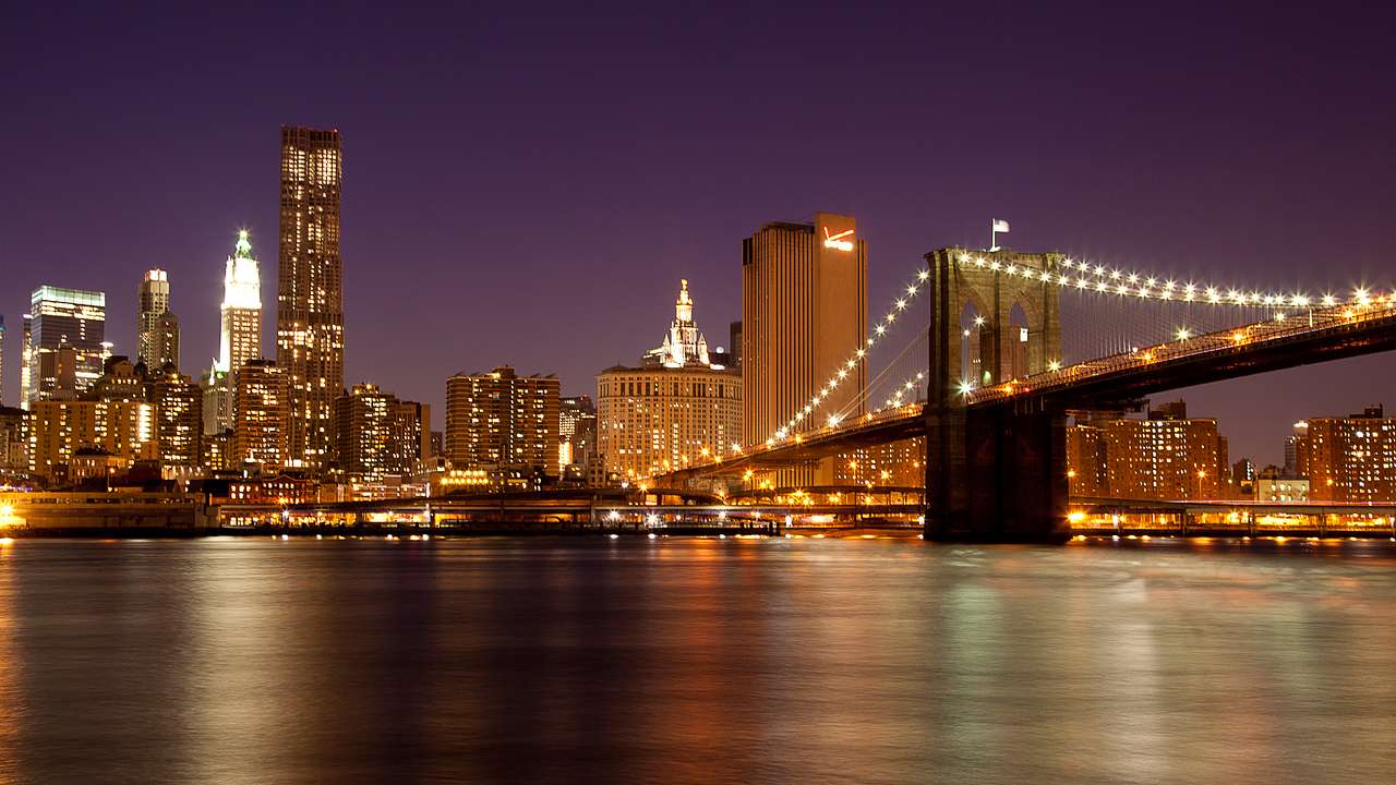 Nighttime view of NYC skyline and the Brooklyn Bridge with water in front
