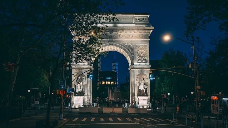 A road with a zebra crossing and trees next to an illuminated stone arch