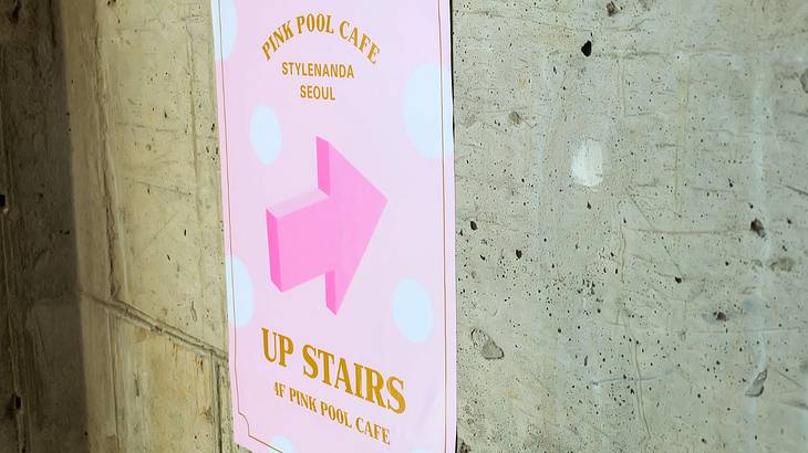 A pink poster with white polka dots stuck to the wall with writings and an arrow mark