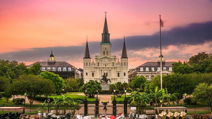 A castle-style building with a park and horse carriages in front under a pink sky